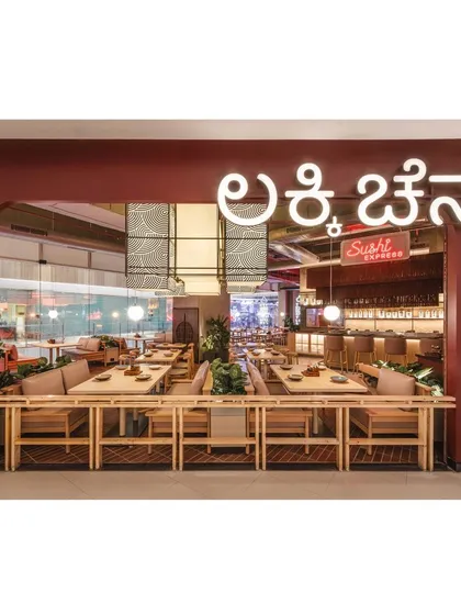 The exterior view showcases the restaurant's name in glowing Kannada script, grounding the international concept with a local touch. The open facade provides a welcoming glimpse into the lively interior.