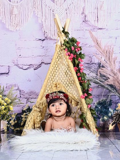 A baby girl peeking out from a bohemian-style teepee setup.