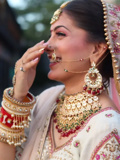 A candid, happy moment of a bride in her wedding attire. She is wearing a heavy Kundan and ruby necklace set with a matching nath and maang tikka, showing the joy my collection brings.
