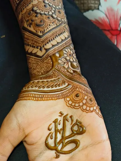 The name 'Hilal' in beautiful, flowing Arabic calligraphy on the palm. The fresh henna paste is so sharp and clean, showing the precision of the script.