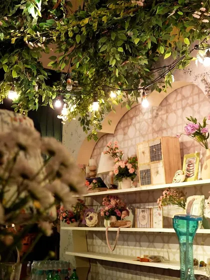 A shelf of decor details illuminated by string lights, with foliage creating a natural canopy.