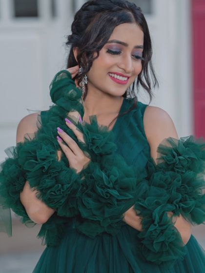 A smiling model shows off the details of the ruffled sleeves and the flattering neckline of this green designer gown.