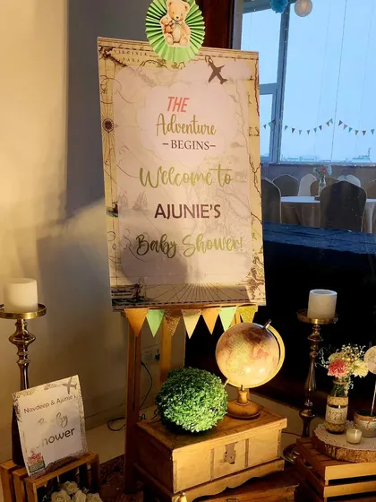 The main welcome board for the baby shower. The vintage map design, combined with a globe, candles, and floral arrangements on wooden crates, creates a beautiful and thematic entrance.