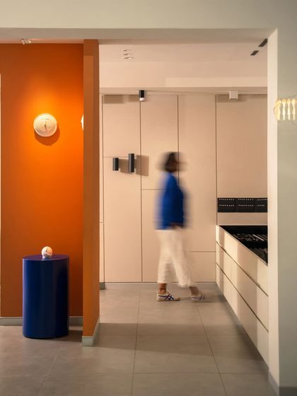 A bright orange accent wall highlights a simple wall sconce, showing how even the smallest fixture can be made a hero. The cobalt blue side table adds another layer of playful, contrasting color.
