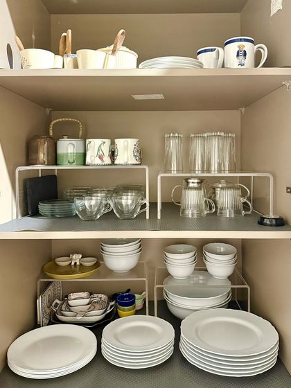 This cabinet uses white metal risers to create extra shelving for plates and bowls. This is a cost-effective and practical way to double your storage space.