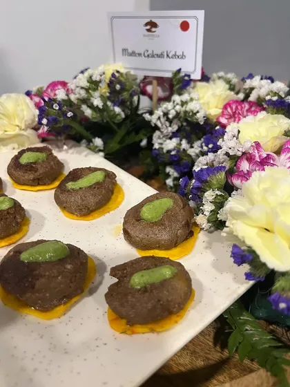 Mutton Galouti Kebabs served on saffron-infused crackers, a sophisticated appetizer for a corporate client. The "non-veg" indicator on the food tag is a small but important detail for guest convenience.