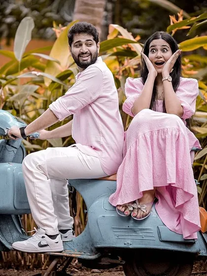 A fun and quirky shot of a couple on a vintage scooter, with the woman making a surprised face, set against a backdrop of lush greenery for a playful pre-wedding photo.