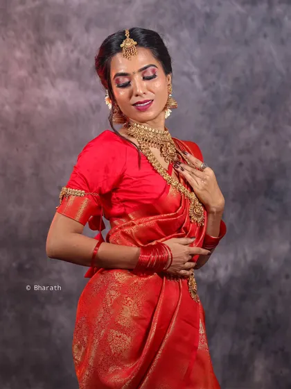 An expressive studio portrait of a model in a red bridal saree, with her eyes closed. This image conveys a sense of serenity and highlights the flawless makeup and traditional jewelry.