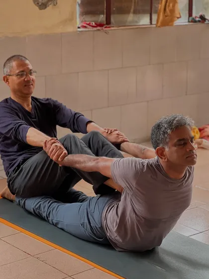 Two students work together to achieve a deeper backbend in the bow pose. This collaborative approach is a hallmark of our community focused teacher training programs.