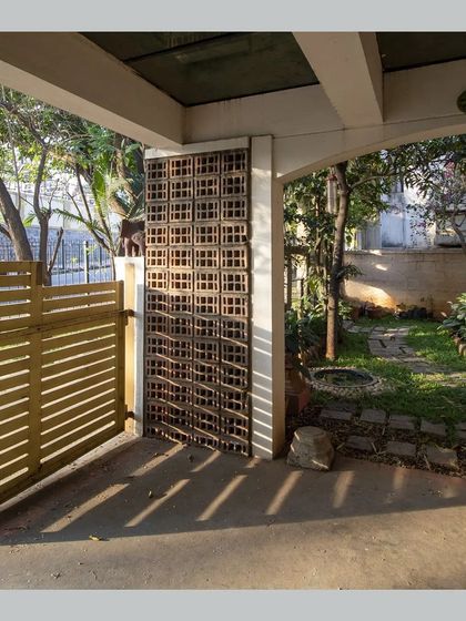 The car porch features jaali walls that allow for light and ventilation, with sunlight creating patterns on the floor.