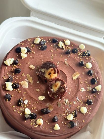 A decadent chocolate bento cake topped with Ferrero Rocher, chocolate chips, and gold sprinkles. A dream come true for any chocolate lover.