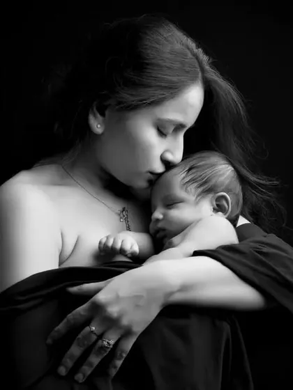 An intimate black and white close-up of a mother's gentle kiss on her newborn's forehead. Our newborn photography focuses on capturing the profound love and delicate details of these fleeting early days.