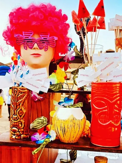 A quirky and colorful sundowner bar setup. The mannequin head with a pink wig and fun glasses is a playful centerpiece that gets people talking.