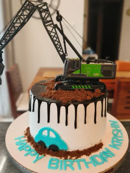 A construction themed cake with a crane digging into chocolate "dirt" and a rich chocolate drip.