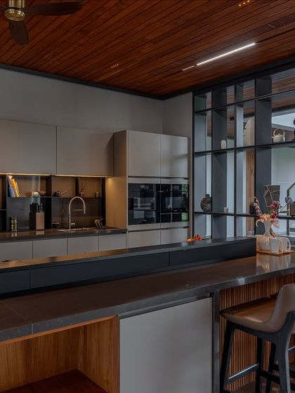 The open-concept design of this kitchen connects it to the living space, separated by a glass and metal shelving unit. The kitchen's neutral palette ensures it complements the home's overall aesthetic.