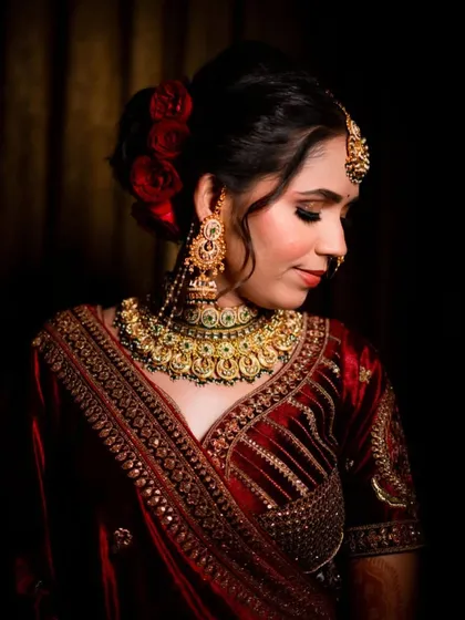 A beautiful portrait of a bride in a velvet lehenga, with a classic red rose bun hairstyle. The makeup is soft and romantic.