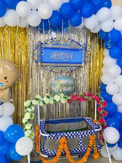 A naming ceremony decoration in blue and white, featuring a balloon arch, a shimmer curtain, and a decorated cradle.