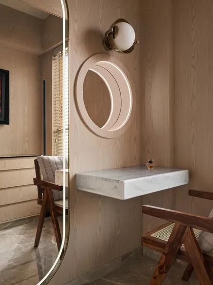 The dresser area in the master bedroom features a custom floating Carrara marble vanity table and a side-lit circular mirror. A tall, backlit mirror provides additional storage, while the classic Pierre Jeanneret chair adds warmth and timeless style.