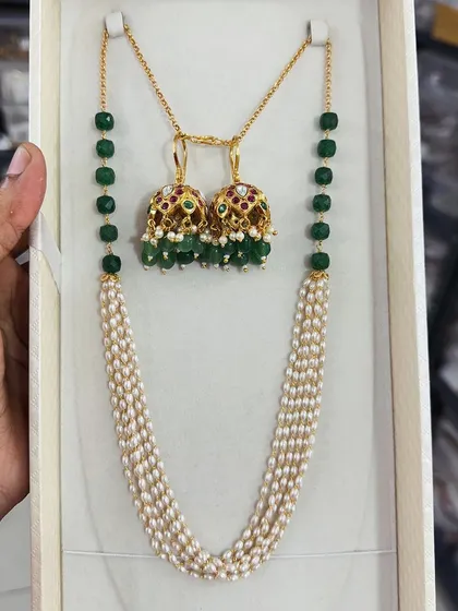 A beautiful combination of green beads and pearls, this set features a multi-strand pearl necklace paired with traditional jhumki earrings. The green beads add a lovely pop of color.