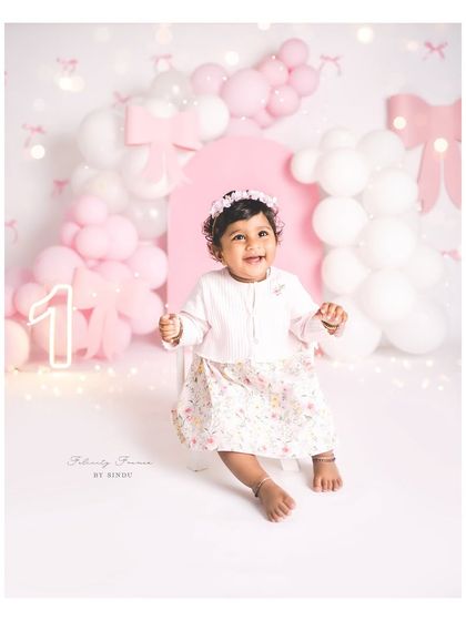 A radiant smile for her first birthday. The soft pink and white bow theme creates a delicate and beautiful backdrop for her special day.