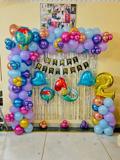 A mermaid-themed second birthday party with a colorful balloon arch against a silver tinsel backdrop.