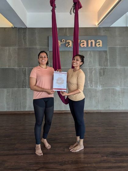 An instructor proudly presents a certificate to a new graduate of the aerial yoga teacher training course.