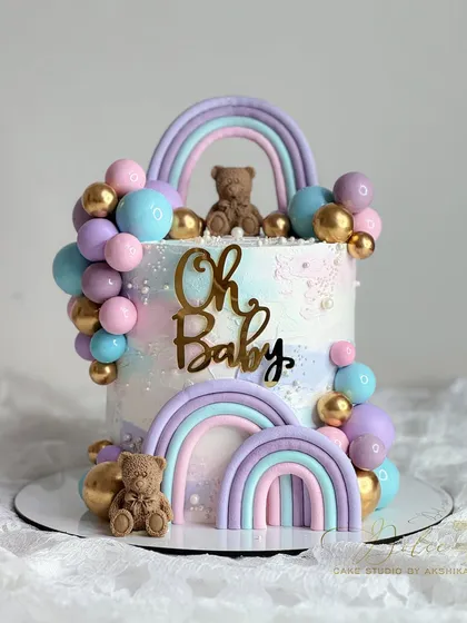 A "Oh Baby" shower cake with pastel rainbows and cute teddy bears. This combines smooth fondant work with piped details and chocolate spheres.