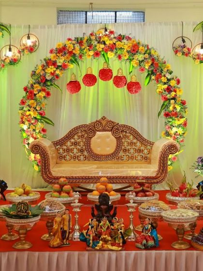 A beautiful baby shower setup with a floral arch and hanging decorative elements. The stage is filled with a complete arrangement of traditional plates, dolls, and a beautiful sofa.