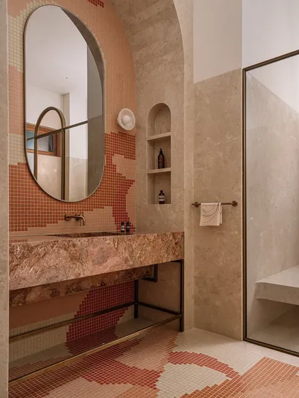 This bathroom is all about playful geometry, with pixelated mosaic tiles in earthy tones creating a dynamic pattern on the floor and walls. The design is anchored by a sculptural pink marble vanity, creating a space that is bold and full of personality.