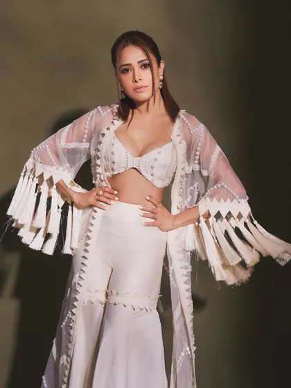 Pearls and tassels make this white indo-western outfit on Nushrratt Bharuccha truly special. The fringed jacket adds a playful, bohemian touch to the elegant sharara set.