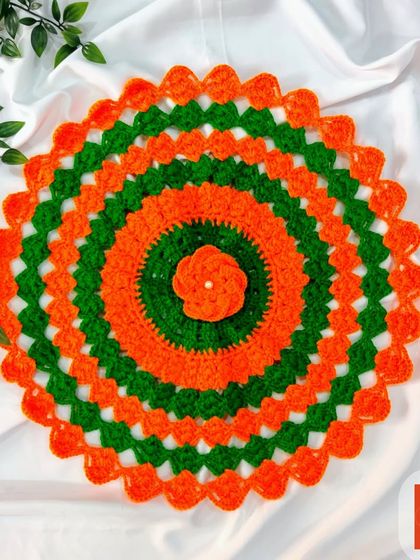 A unique doily in orange and green with a small flower at the center. The scalloped edges add a delicate touch.