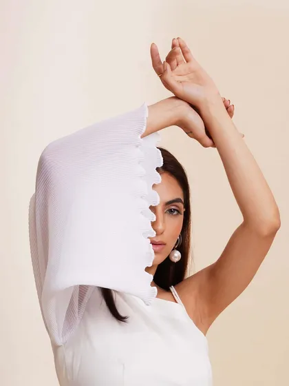 An artistic pose where the model uses the voluminous sleeve of her top to frame her face. This creative shot highlights the garment's unique texture and design.