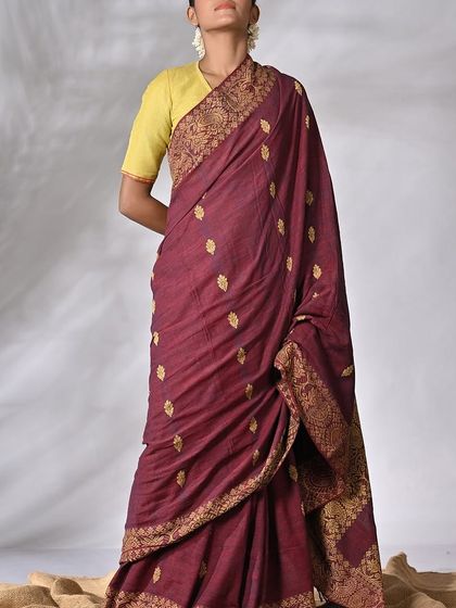 A model draped in an elegant maroon handwoven sari with intricate gold motifs, a timeless piece of heritage.