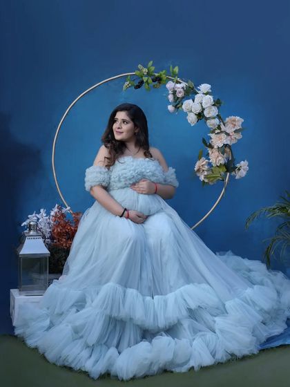 A fairytale moment. Seated in a flowing blue gown against a matching backdrop with a floral hoop, this portrait is the picture of elegance and grace.