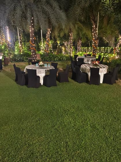 The guest seating area at the outdoor Diwali party, with tables set up on the lawn under trees decorated with fairy lights.
