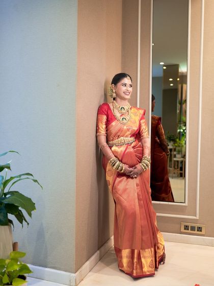 The bride posing in her gorgeous red and gold Kanjivaram saree. The makeup is kept elegant and classic to complement the richness of her attire.