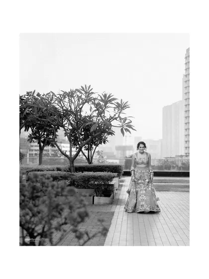 A solitary portrait of the bride in her beautiful lehenga, captured in black and white against an urban garden backdrop. A moment of quiet elegance before the ceremony.