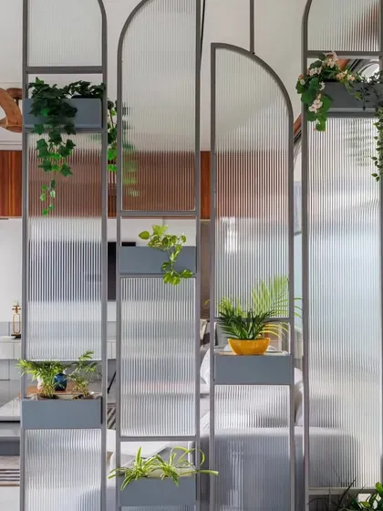 This is a creative partition solution using fluted glass and metal frames with built-in planters. It elegantly divides the space while allowing light to pass through and adding a touch of greenery.