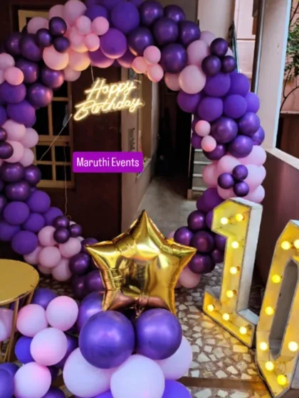 A 10th birthday party with a purple and pink circular balloon arch. The setup includes a neon sign and large, light-up marquee numbers.