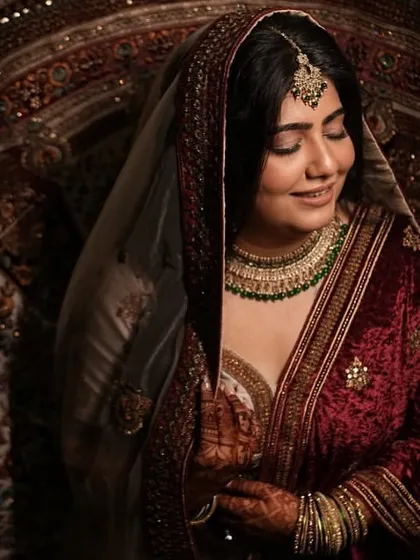 A dramatic and artistic portrait of the bride. The lighting highlights the richness of her velvet outfit and the soft glow of her makeup.