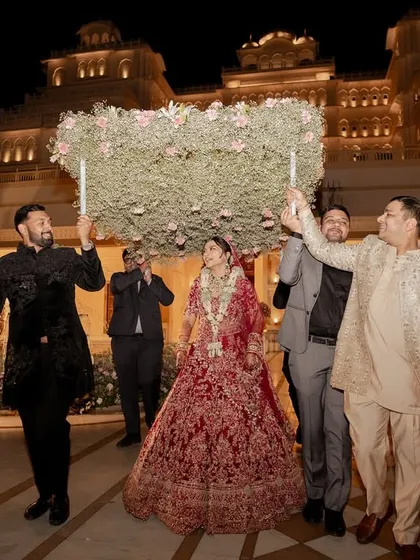 The bride makes her grand entrance under a phoolon ki chaadar, with a magnificent palace lighting up the night sky. This is a moment of pure fairytale magic, a core memory from a royal Indian wedding.