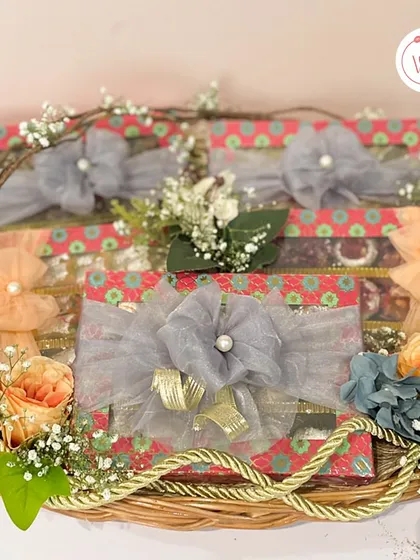A wicker basket filled with colorful mithai boxes, each tied with a unique floral-inspired ribbon.