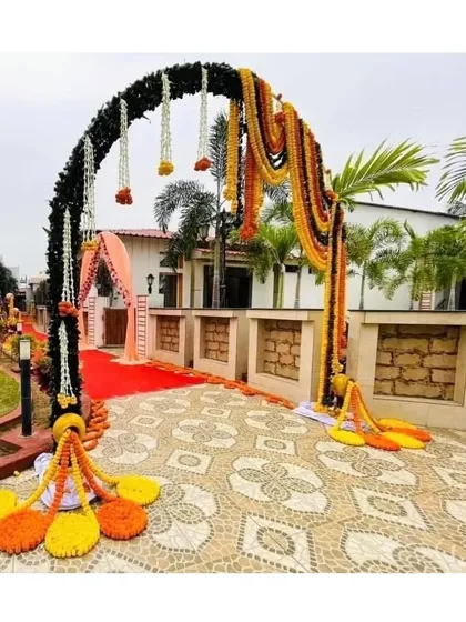 This grand entrance arch for an outdoor wedding in Pune uses a mix of dark foliage and hanging marigold garlands, creating a rustic yet festive gateway for guests walking the red carpet.