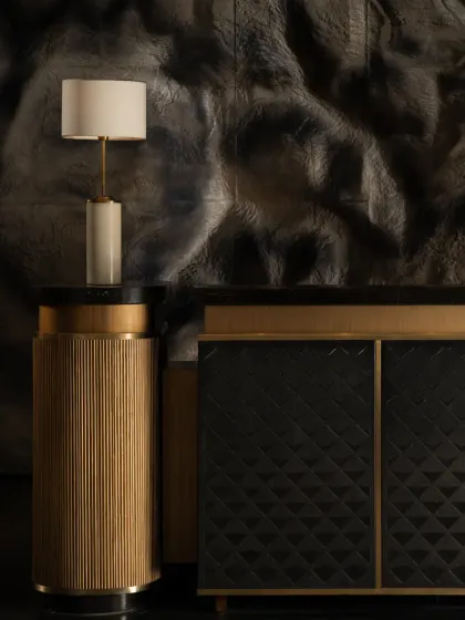 A close-up of the reception area at the Soaltee Hotel. The custom fluted brass podium lamp stands in contrast to the textured, mountain-inspired wall and the geometric pattern of the console, creating a composition of refined details.