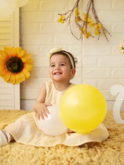 A joyful first birthday shoot with a sunny yellow theme. This little girl is all smiles as she plays with balloons on a soft yellow rug.