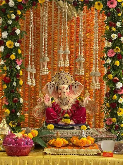 For this Ganpati stage decoration, I used a backdrop of marigold flower strings and framed it with colorful floral garlands. The pearl string hangings add a touch of elegance to the traditional setup.