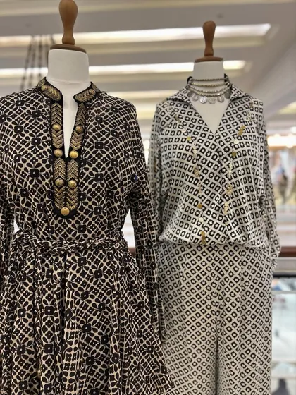 A closer look at two of the black and white outfits, one a belted dress with gold button details and the other a stylish wrap-style jumpsuit.