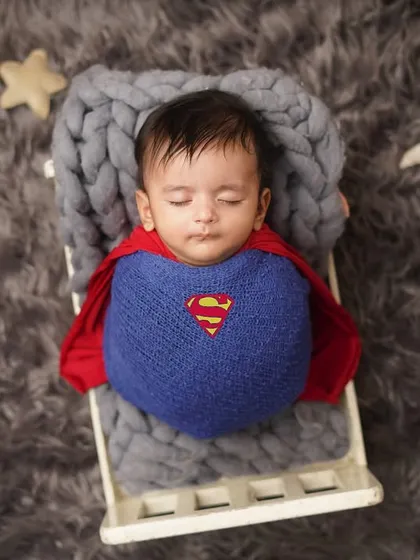 Our little superhero rests in his tiny bed, surrounded by stars. The full setup shows the creative details that go into a themed infant photoshoot.