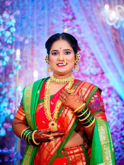 The bride gently touches her necklace in this portrait, drawing attention to her beautiful gold jewellery. Her warm smile and traditional attire complete the classic Maharashtrian bridal look.