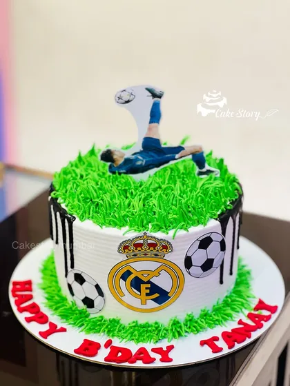 A fantastic Real Madrid football cake for a fan's birthday. The cake features a grass-like green topping, the team logo, and a player doing a bicycle kick.
